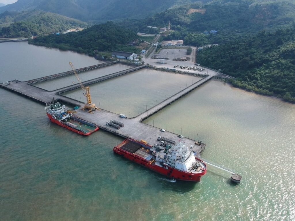 Two red support vessels moored beside a long pier in a bay